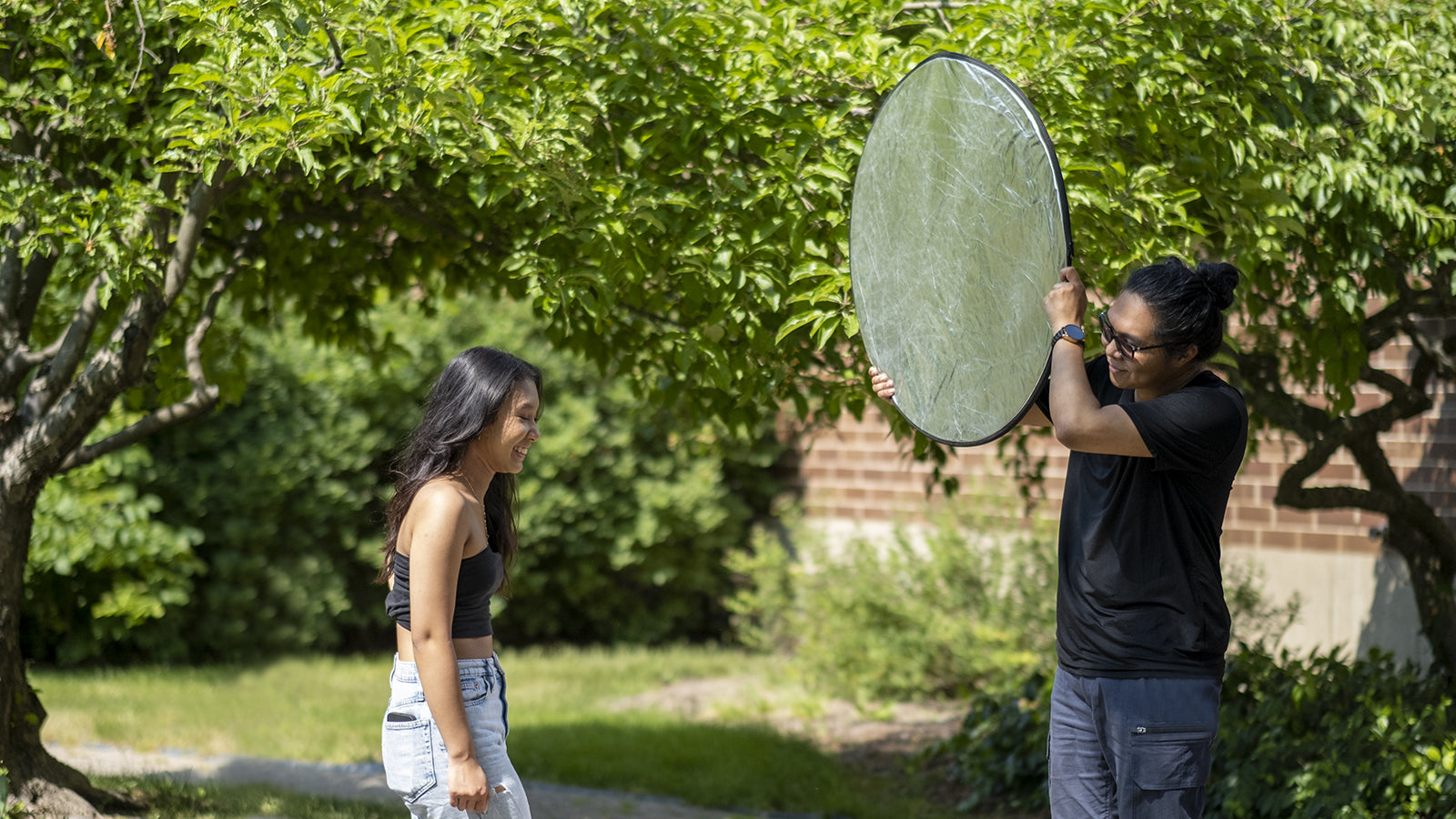 Photographer using a large reflector to light a subject outdoors beneath trees